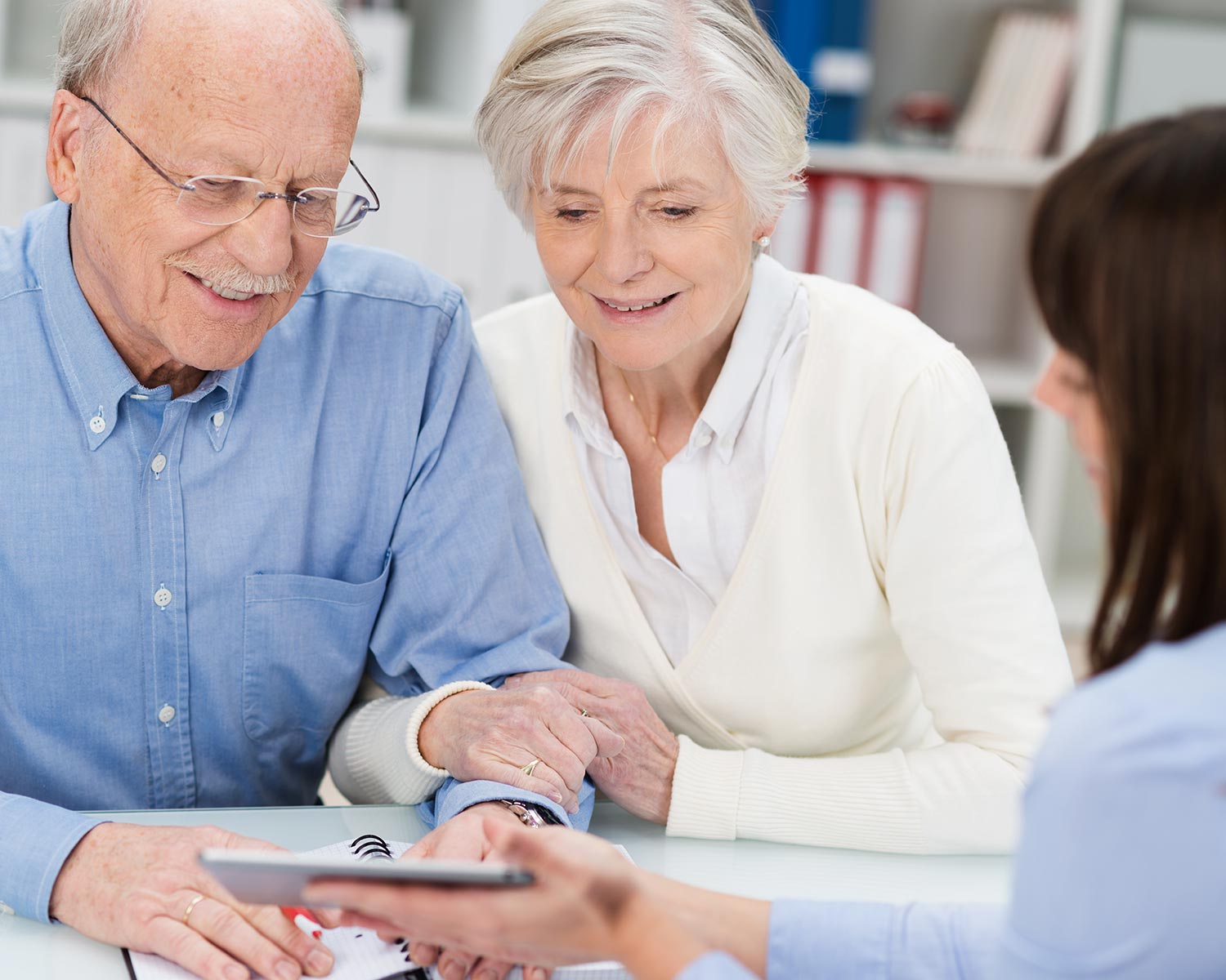Ein älteres Paar betrachtet zusammen mit einer Beraterin ein Dokument auf einem Tablet.